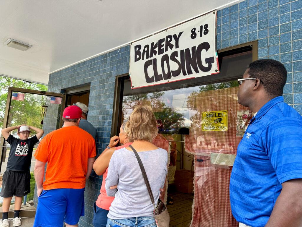 A line of customers waiting to get baked goods under a sign announcing the shop's closing.