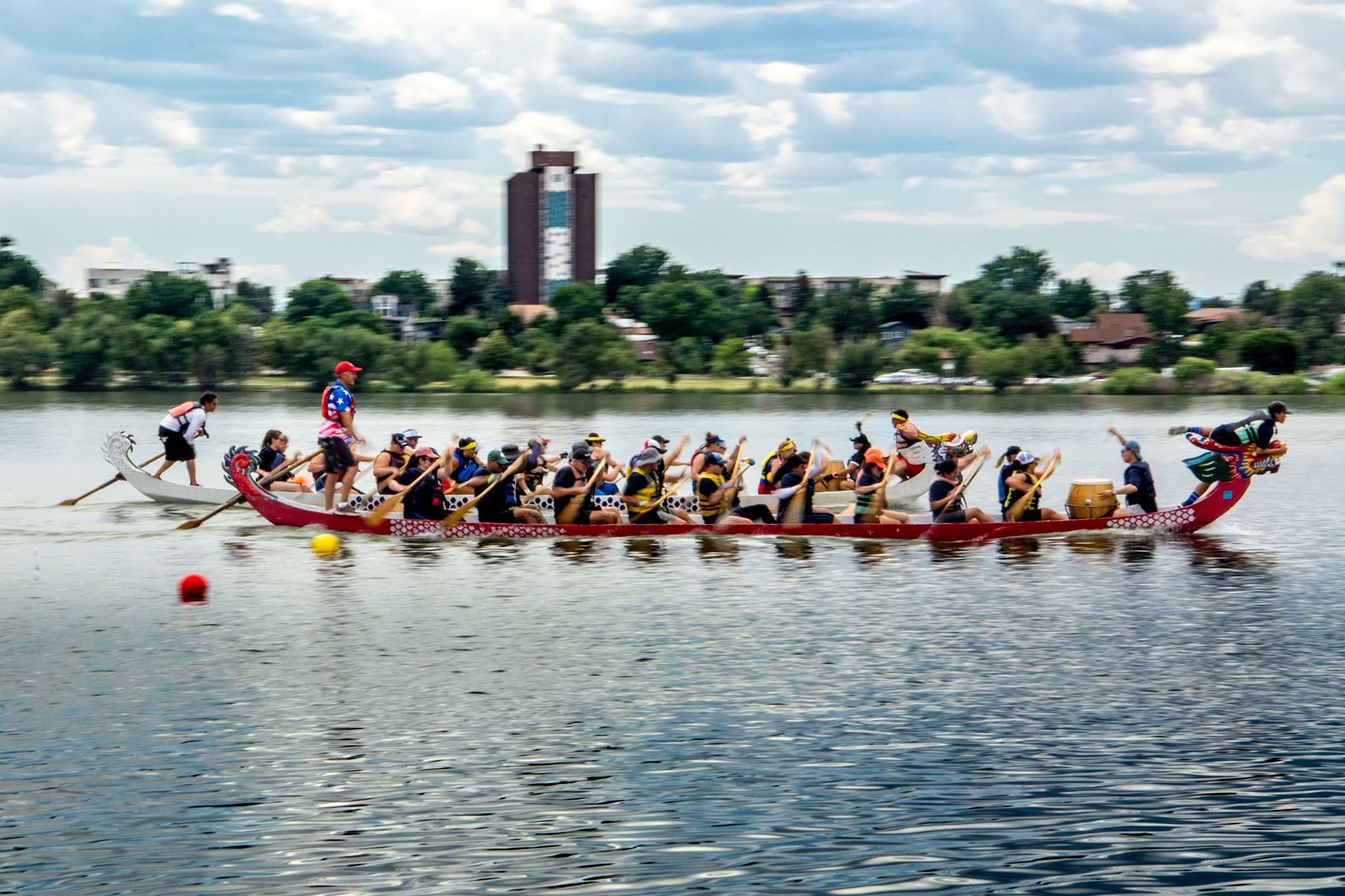 Paddlers race in a boat on a lake with green shrubbery in the distance