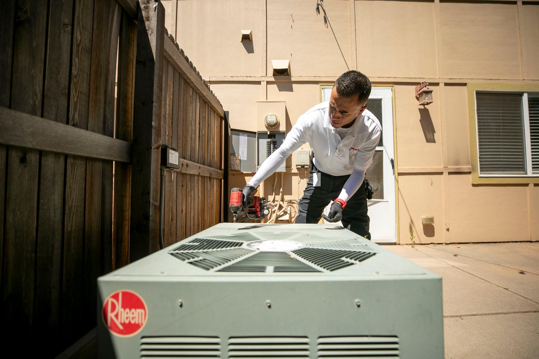 Man leans over an air conditioner unit outside next to a wood fence.