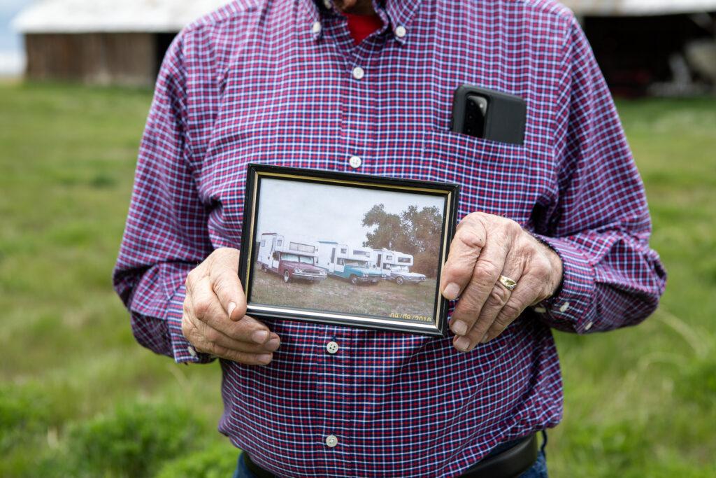 A man holds a photograph of three camper cars in a row.