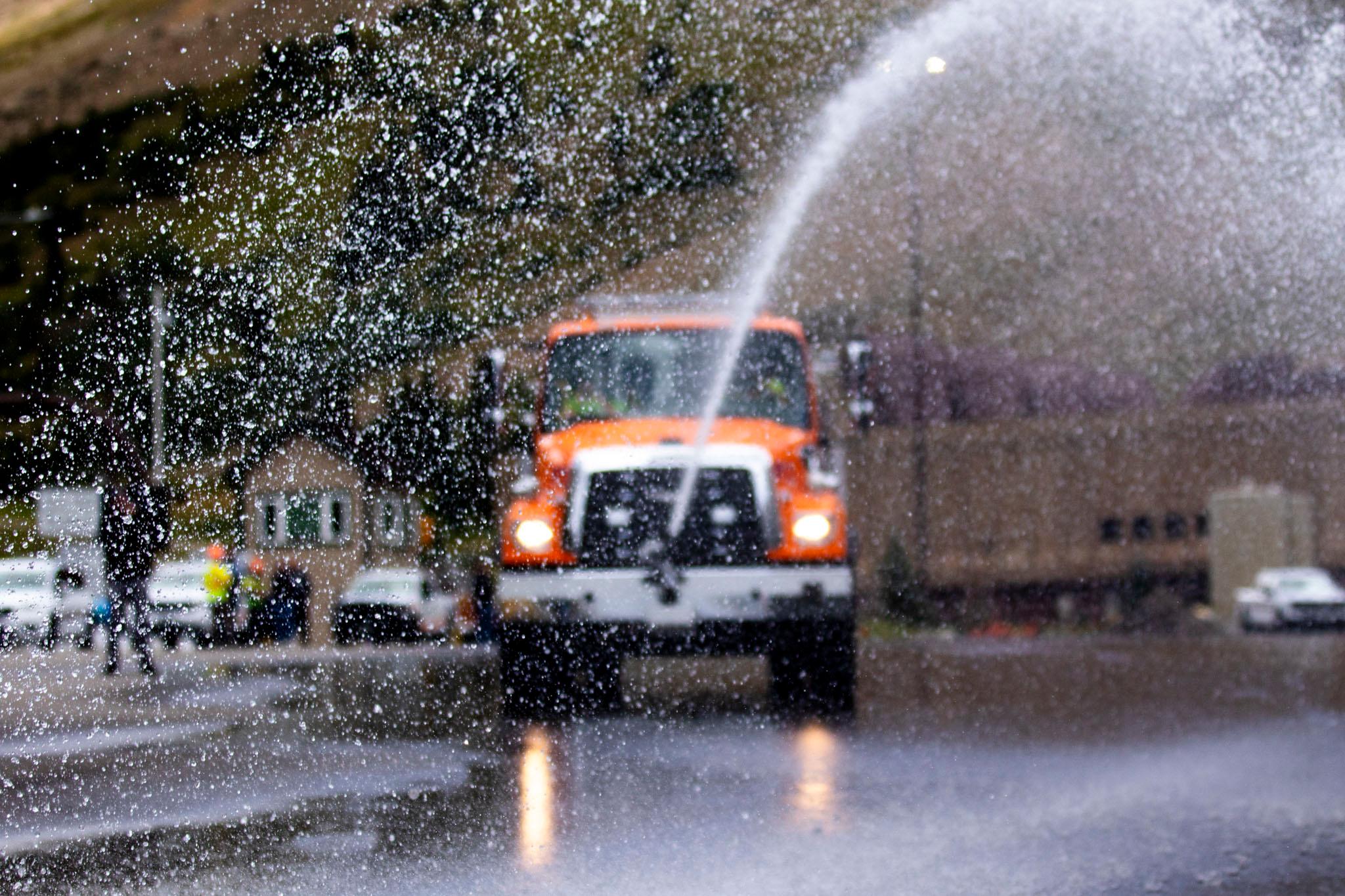 Beads of water are frozen in the air; an orange truck sits in the distance, out of focus.