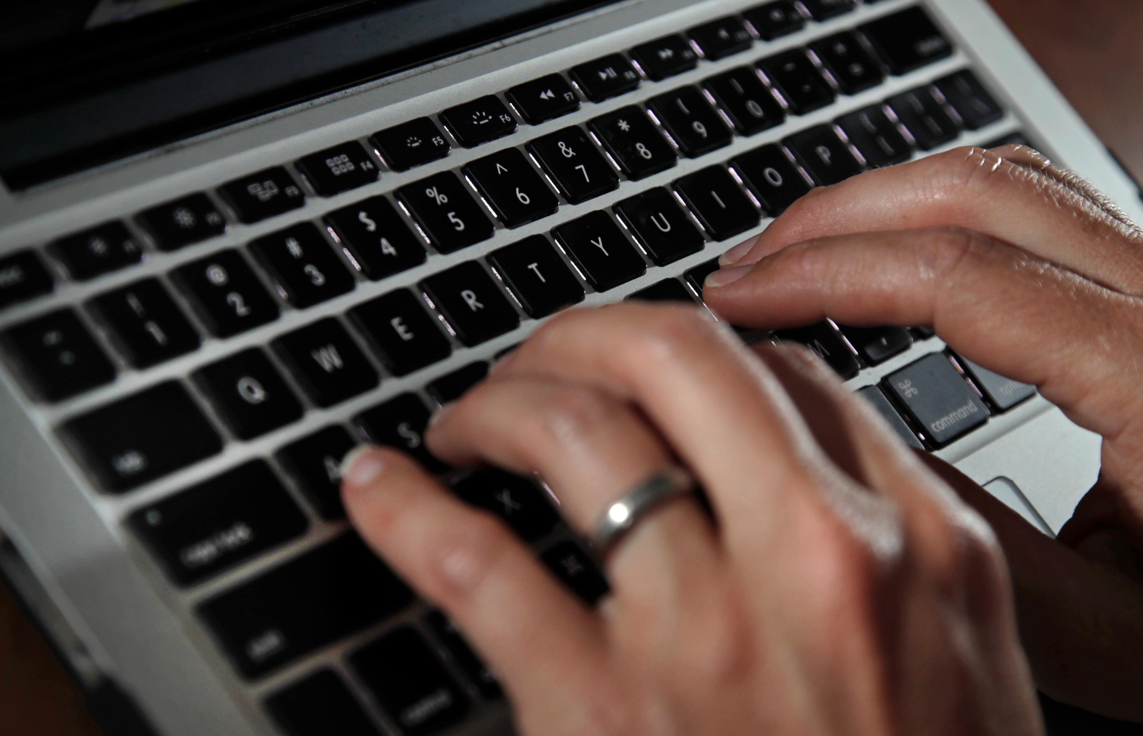 A pair of hands type on a laptop computer keypad.