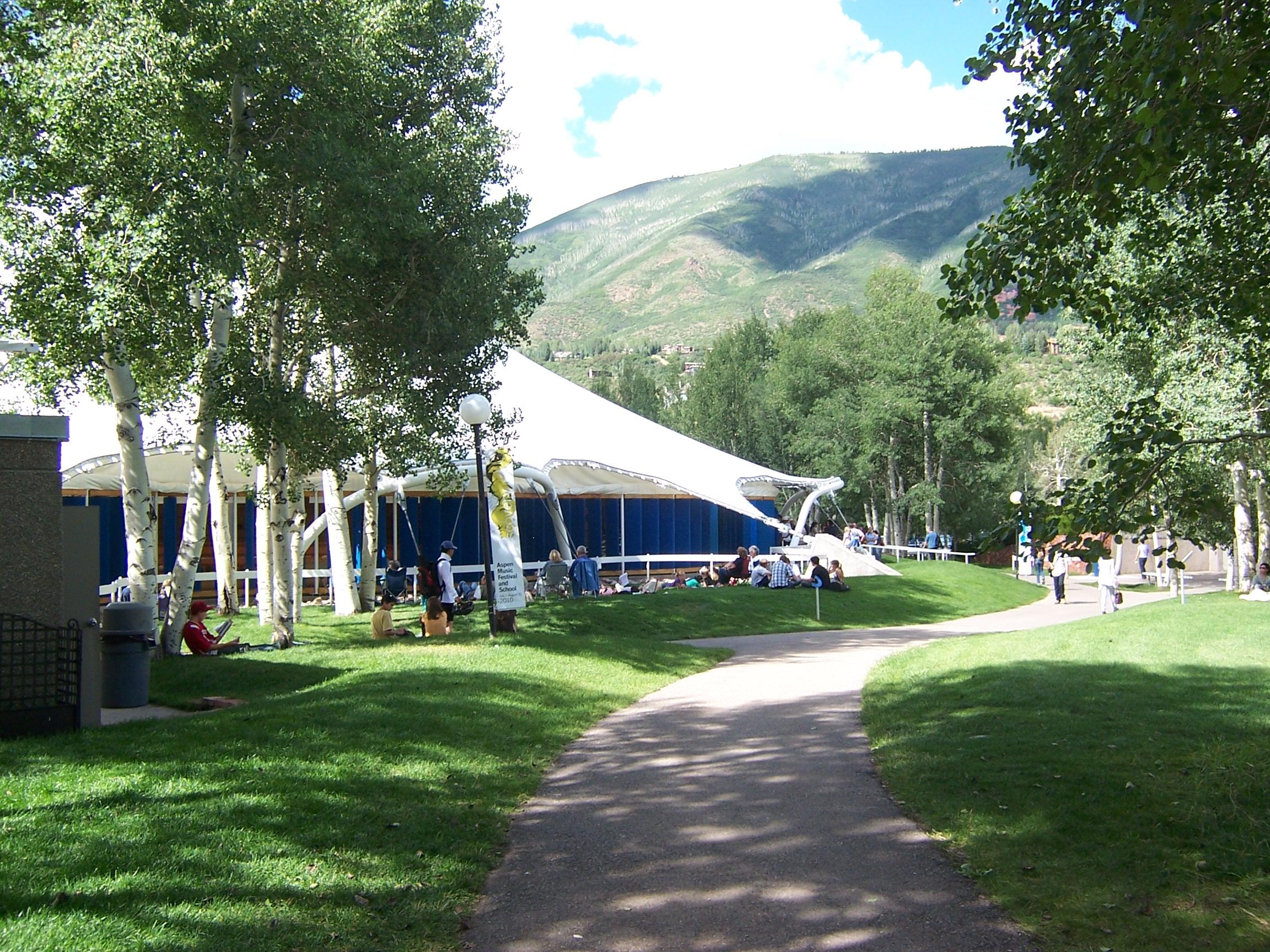 A path curves through a green lawn towards the mountains and the tent at the Aspen Music Festival and School.