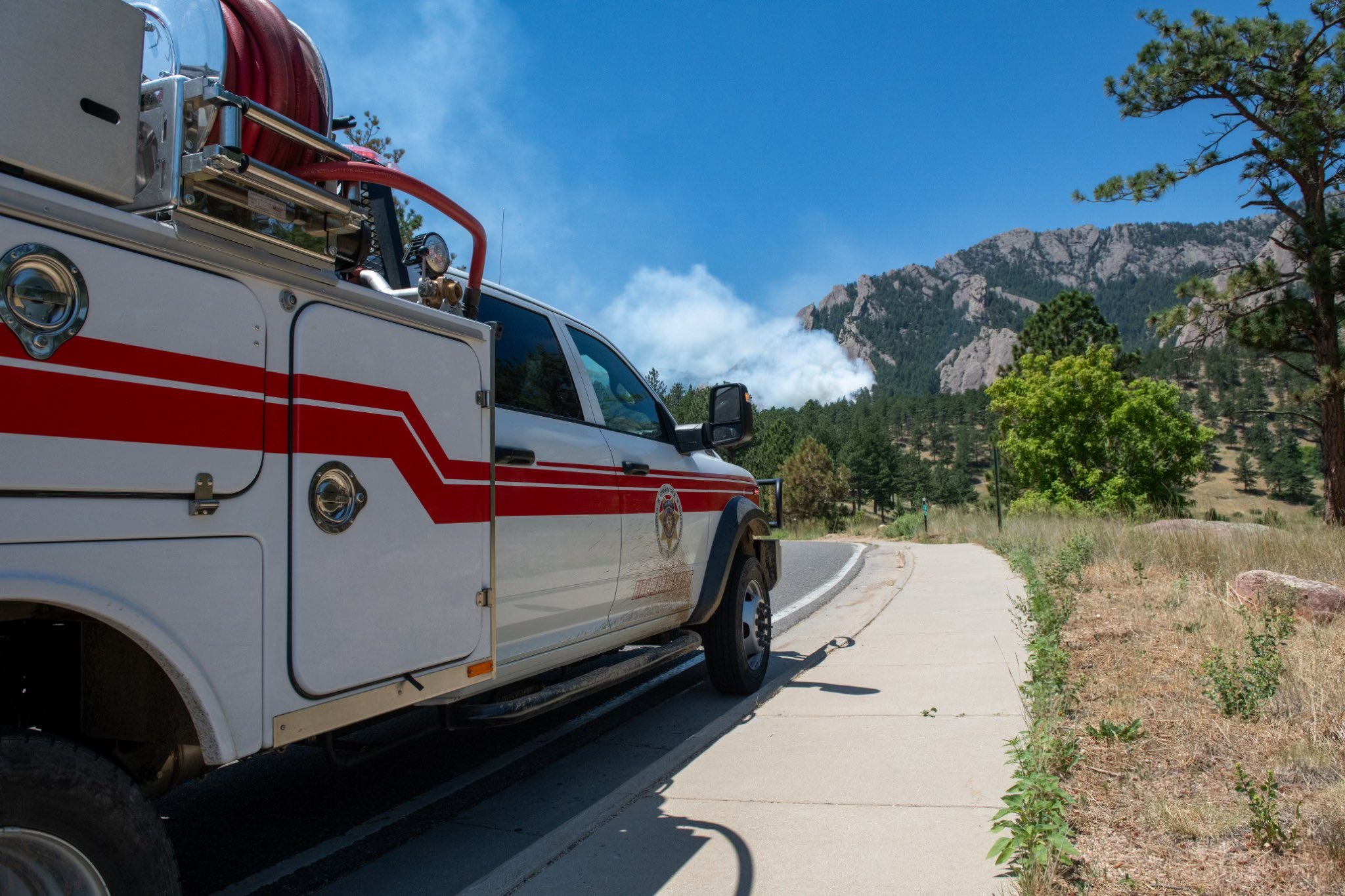 Fire truck pulled off to the side of the road with a view of a smoke plume coming up in the distance.