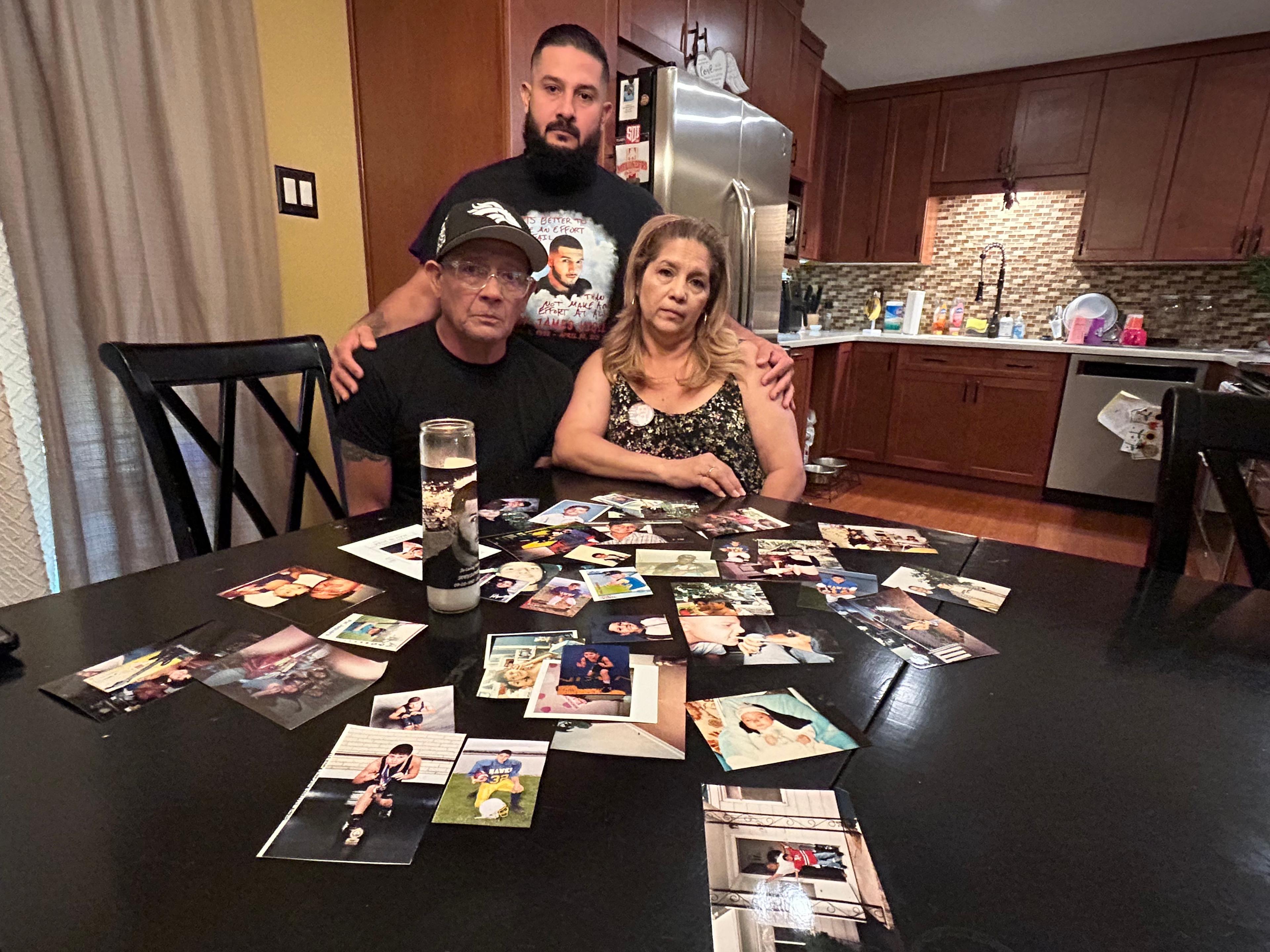 Three family members look down on a table filled with photographs of Joby Vigil, who was killed by Thornton Police after a chase in April, 2024