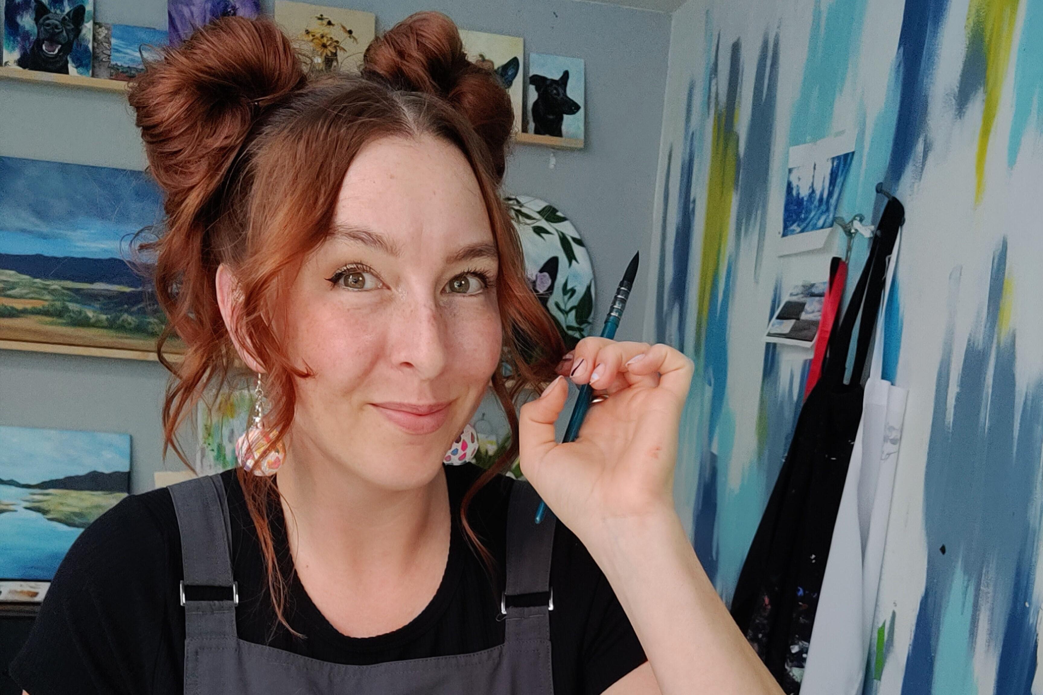 A woman poses in a home studio surrounded by colorful blues and yellows on artworks on the walls around her.