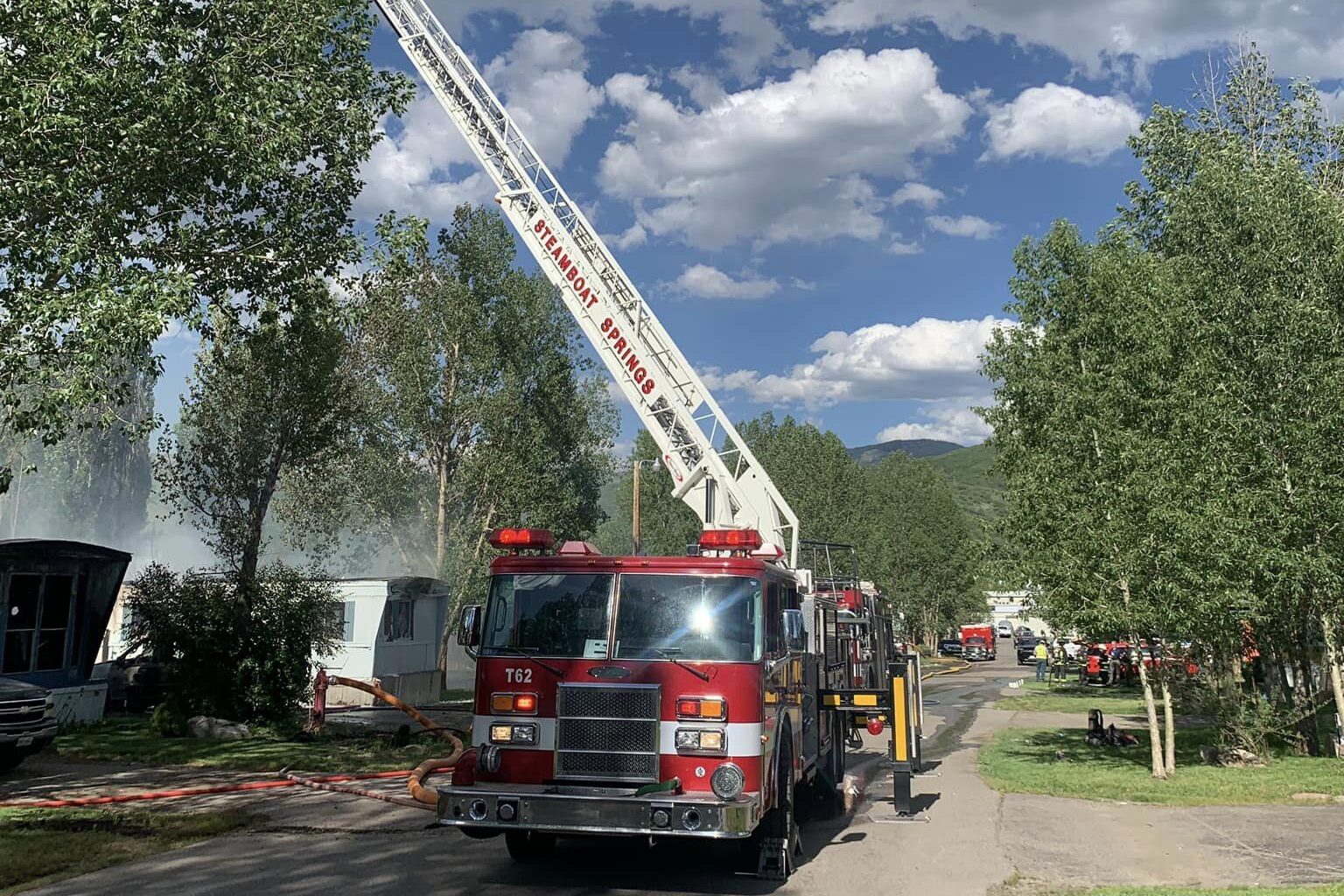 Shows a Steamboat Springs firetruck dousing a fire with smoke rising after a plane crash in a mobile home park.