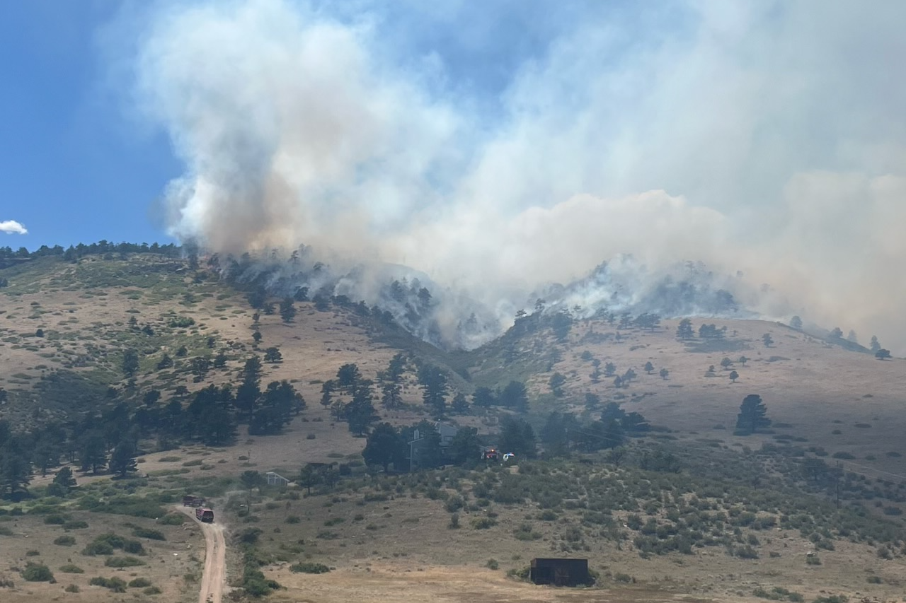 Smoke from the Stone Canyon Fire is visible in the distance in a hilly area.